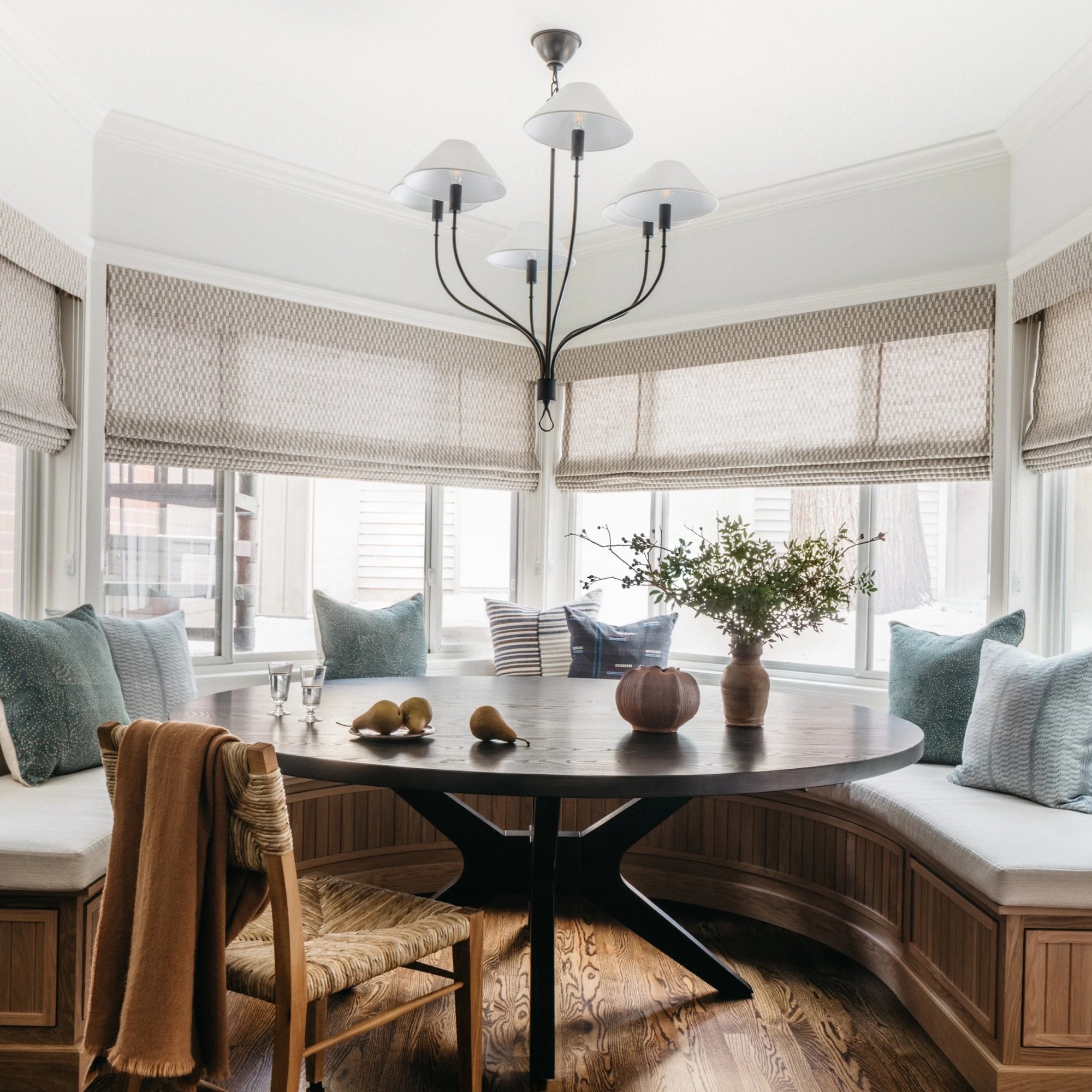 Curved banquette breakfast nook with round wood table and soft blue pillows designed by Leah Phillips Interiors