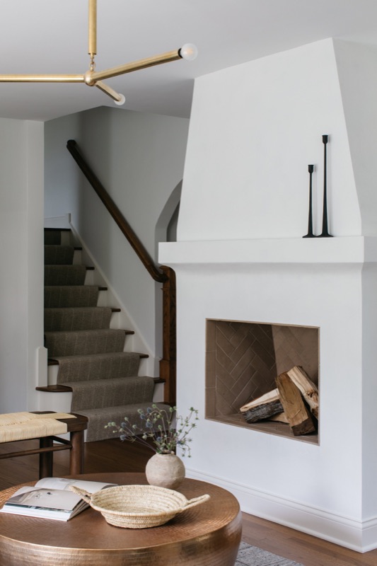 Sculptural plaster fireplace beside a sunlit staircase designed by Leah Phillips Interiors
