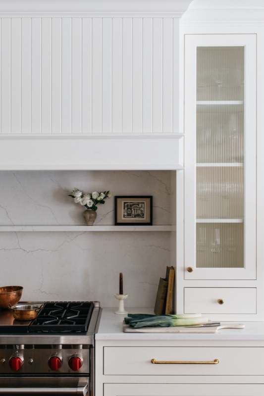 White kitchen range wall with glass-front hutch cabinet designed by Leah Phillips Interiors