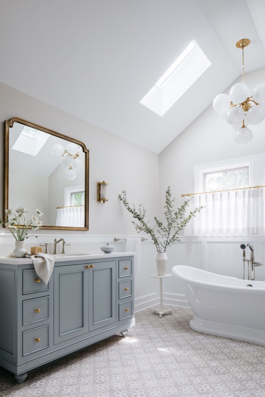 Blue-gray bathroom vanity with skylight and soaking tub designed by Leah Phillips Interiors