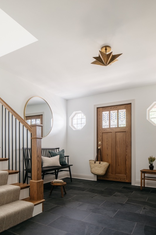 Stair landing with round window and wood entry door · Glenview Home Renovation by Leah Phillips Interiors