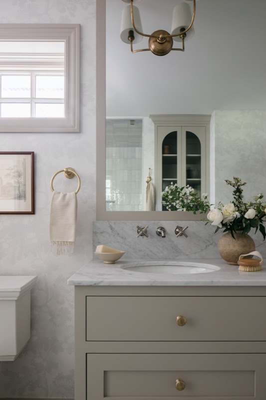 Bathroom vanity in putty tone with glass upper cabinet · Glenview Home Renovation by Leah Phillips Interiors