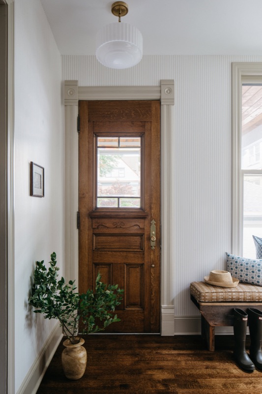 Original wood entry door with bench and potted greenery · Oak Park Main Level Renovation by Leah Phillips Interiors